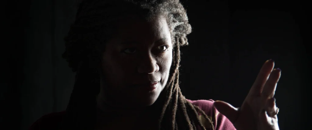 Storyteller Donna Washington, lit from the side, looking engagingly towards the viewer. On page for her performance.