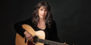 Singer-songwriter Karla Bonoff with her acoustic guitar, looking directly at the camera. For her concert.