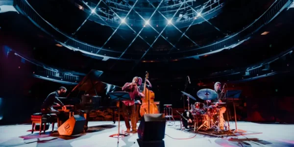 LP & The Vinyl performing jazz on stage with piano, bass, and drums under spotlights. For their concert.