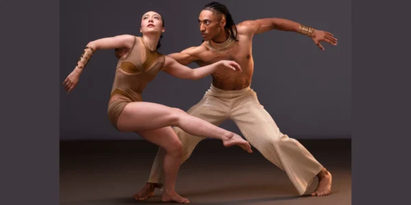 Ailey II dancers in flowing, warm-toned costumes, poised in a powerful contemporary dance move. Context: Ailey II performance.