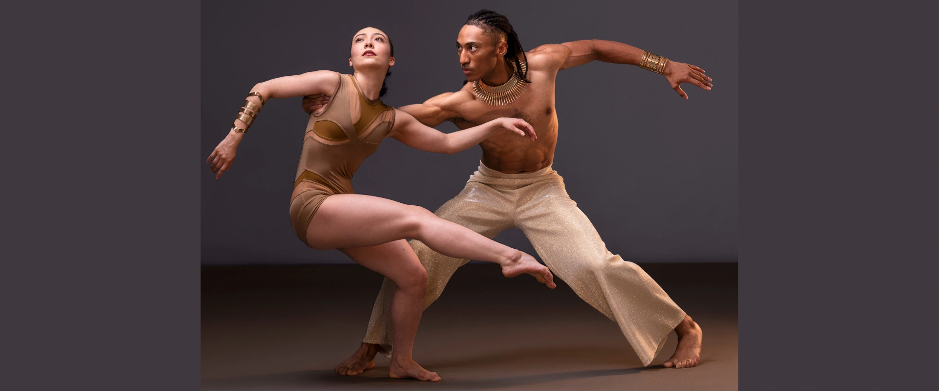 Ailey II dancers in flowing, warm-toned costumes, poised in a powerful contemporary dance move. Context: Ailey II performance.