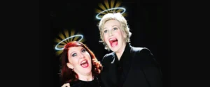 Jane Lynch and Kate Flannery with halos, mouths open in a comedic expression. For "The Trouble with Angels" event.