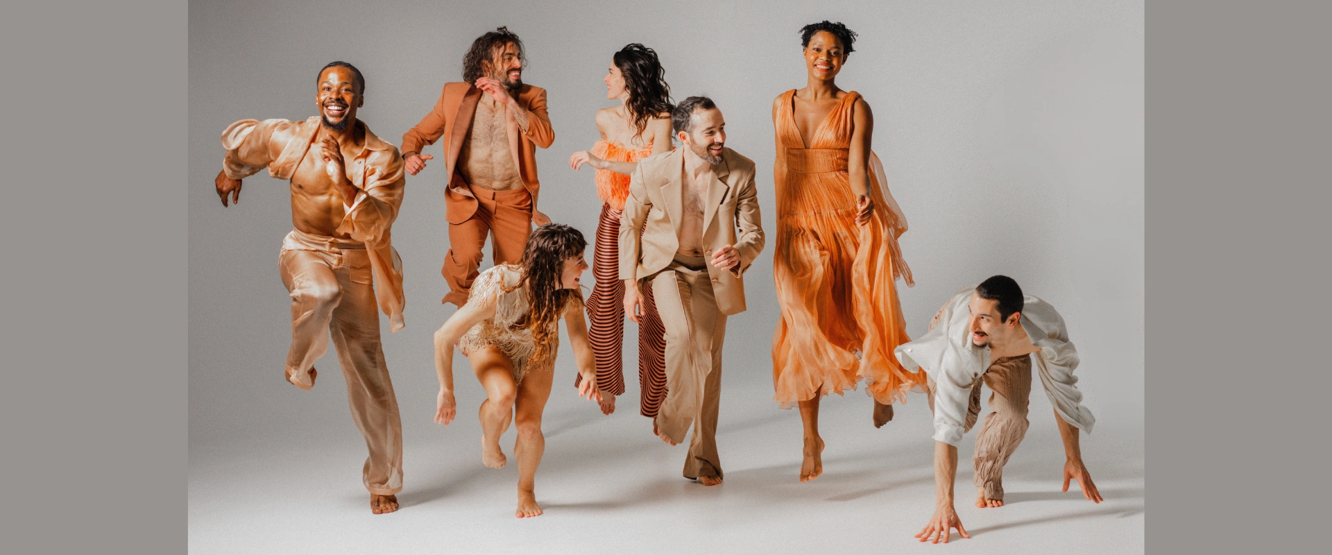 Six BODYTRAFFIC dancers in various contemporary dance movements, some mid-air, in earth-toned outfits.