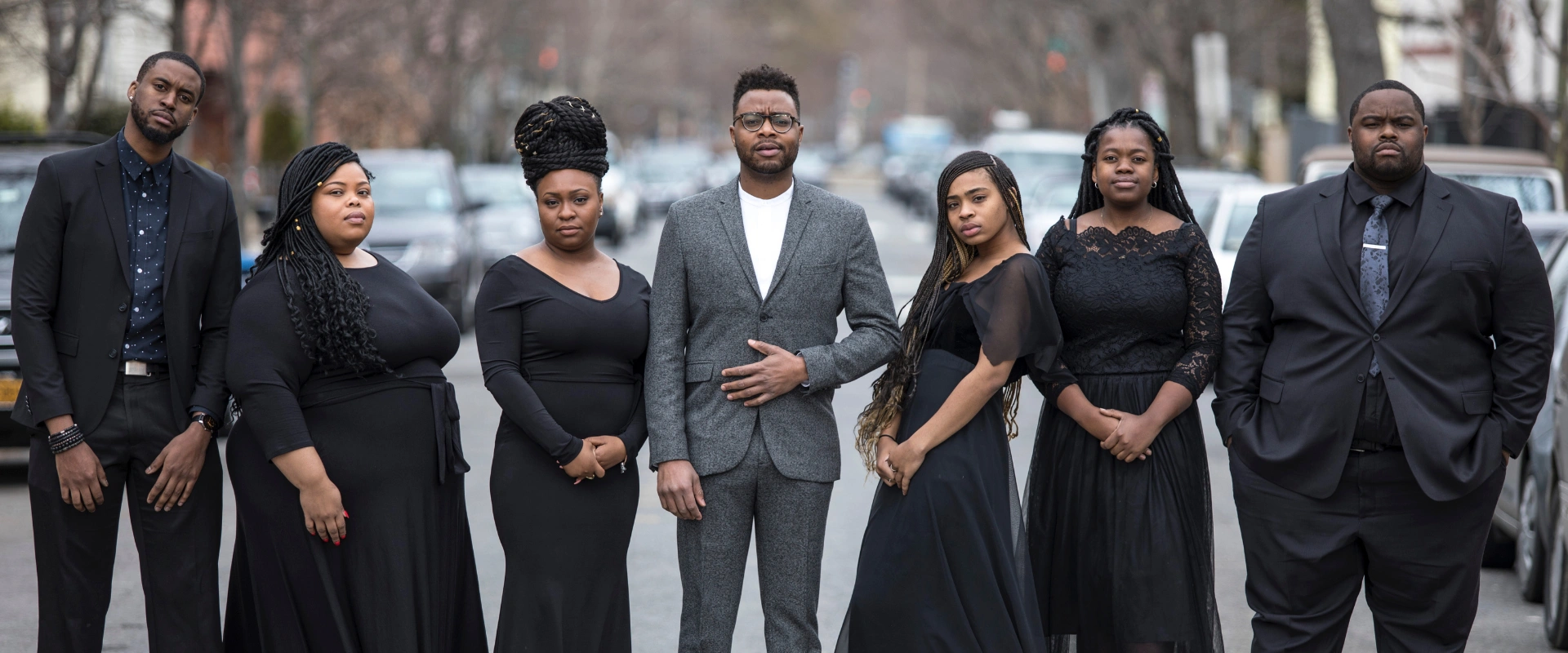 Reginald Golden in a grey suit, flanked by six singers in black dresses and suits on a street. Context: 