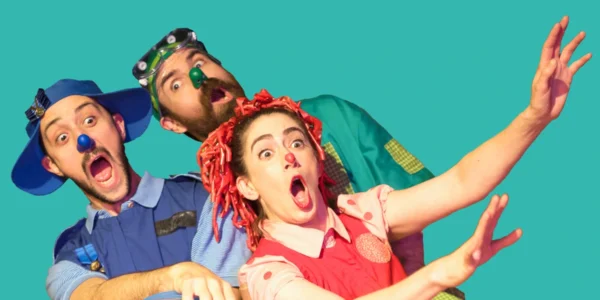 Three performers in colorful, whimsical costumes and clown noses with exaggerated, surprised expressions. On page for Yellow Bird Chase.