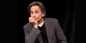 Robert Dubac on stage, chin resting on hand, with a thoughtful, slightly confused expression. For his comedy show.