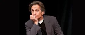 Robert Dubac on stage, chin resting on hand, with a thoughtful, slightly confused expression. For his comedy show.