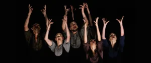 Eight dancers reaching upwards with expressive faces on a dark stage. On page for Stewart/Owen Dance + Guests.