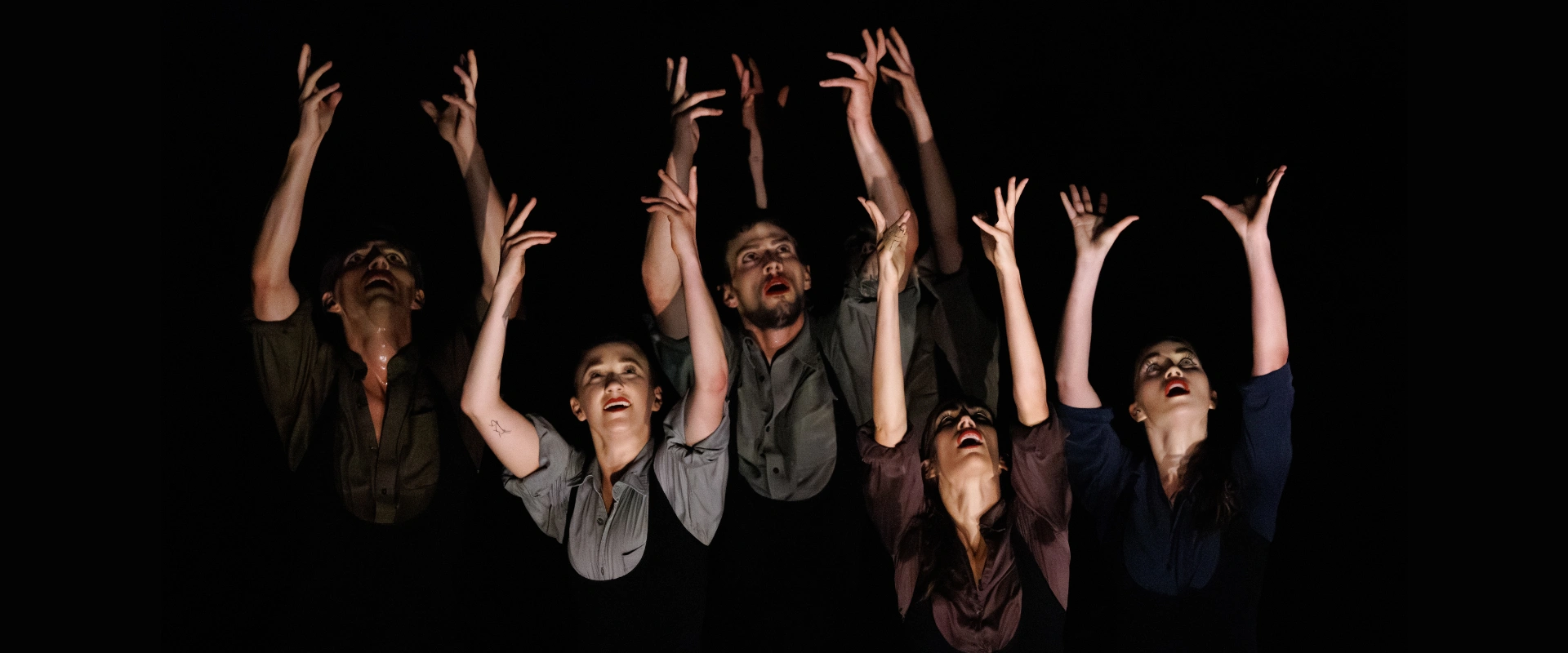 Eight dancers reaching upwards with expressive faces on a dark stage. On page for Stewart/Owen Dance + Guests.