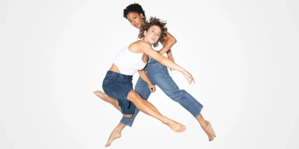 Photo: two dancers from BODYTRAFFIC in bright white shirts and jeans, posed jumping in mid-air